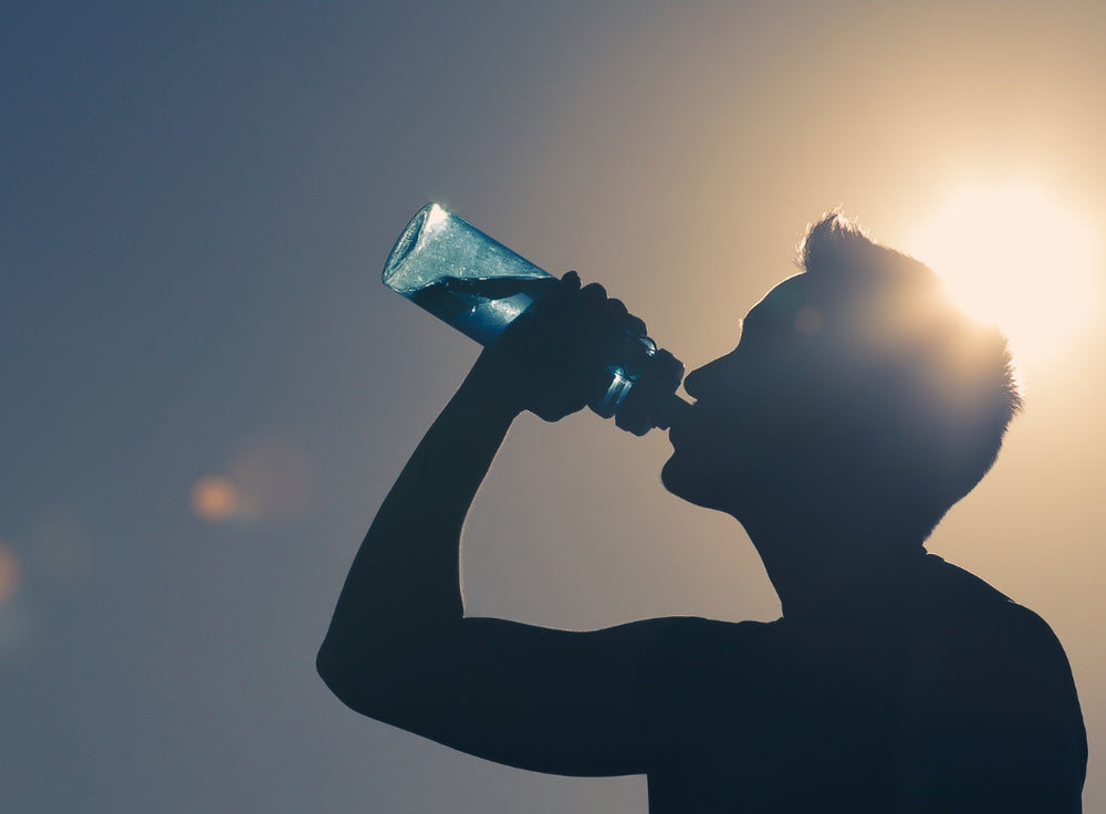 Stockphoto mit Mann der Wasserflasche angesetzt hat und frisches Wasser trinkt mit Sonnenschein als Gegenlicht