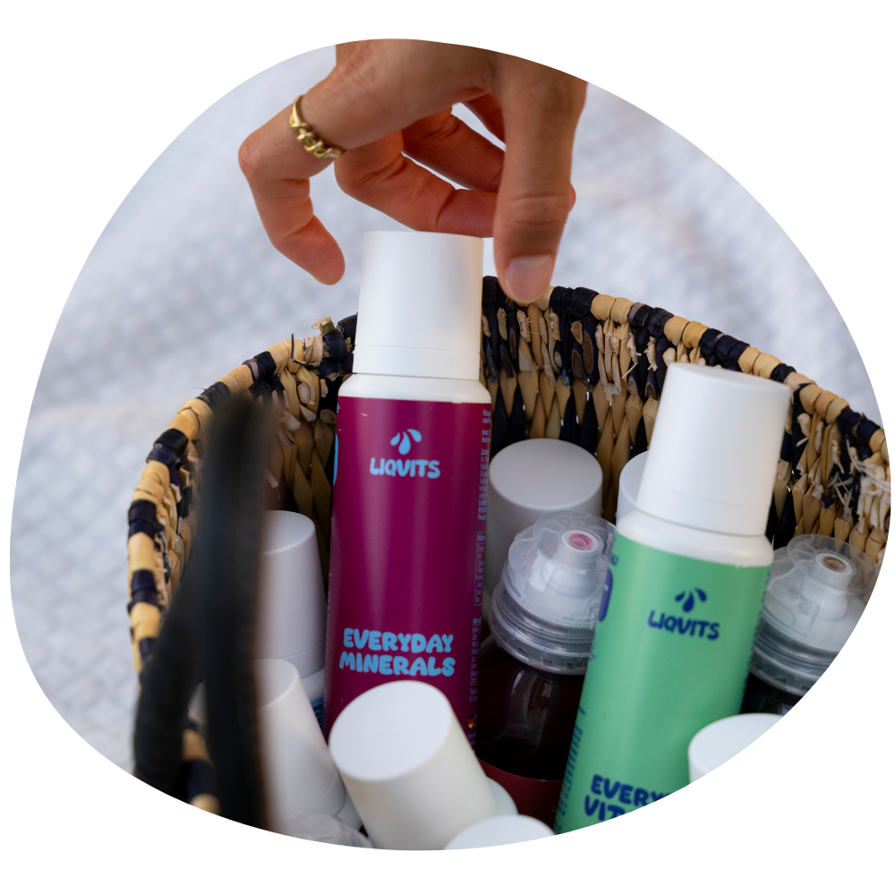 LiqVits Everyday Minerals und Everyday Vitamins mit Sirupflaschen in einem Korb und einer Hand die danach greift