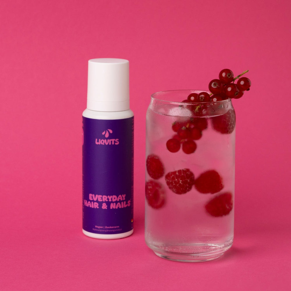 LiqVits Everyday Hair & Nails neben einem Glas Wasser mit Früchten Himbeeren und Johannisbeeren